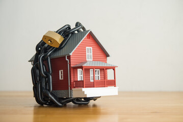 House in chain with padlock on wooden table white wall background copy space. Asset forfeiture,...