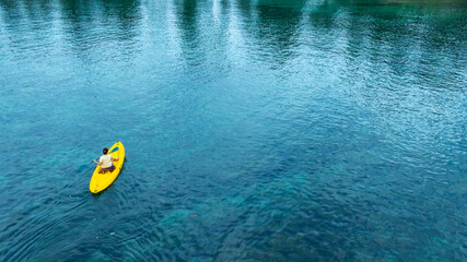 Aerial view woman bright yellow kayak with in the vast expanse of crystal clear turquoise water. The seabeds rocky texture is visible beneath the surface, concept marine environment