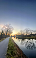 A tranquil and peaceful canal scene unfolds at sunset, showcasing trees and their reflections in...