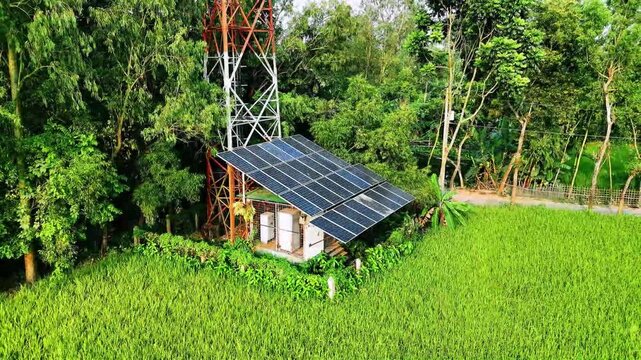 Aerial drone view of solar power system with mobile tower in rural Bangladesh surrounded by lush green fields