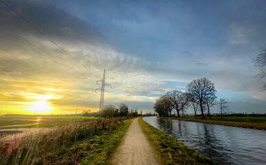 A stunningly picturesque sunset view that beautifully illuminates a calming canal path surrounded...