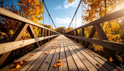 Wooden suspension bridge in autumn forest with scenic view, fall foliage, and sunlight.