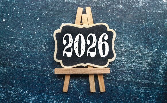 A small wooden chalkboard with the words 2026 written in white chalk isolated on gray background. Welcome a Fresh Start in 2026.