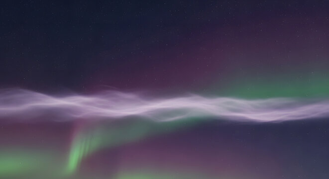 Vibrant green and purple aurora borealis illuminating the night sky with wavy light formations and vertical streaks of light.