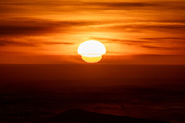 Dramatic orange distorted sun setting into the ocean. A sunset mirage