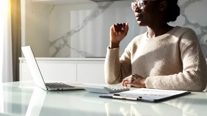 African american woman working from home with laptop calculator and documents in bright sunlight analyzing financials - Powered by Adobe