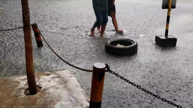 Heavy rainfall causes street flooding with pedestrians wading through water barefoot