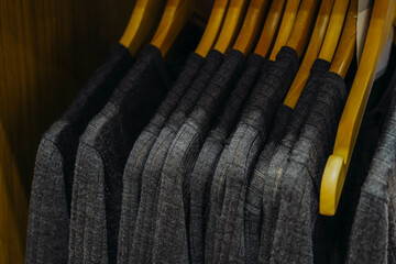 Multi-colored warm knitted sweaters hang on wooden hangers in clothing store.