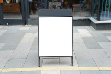 Blank white outdoor advertising stand or sandwich board mock up template. Clear street signage board placed by an outdoor dinning area of a restaurant. Background texture of standee on street.