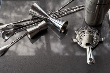 Stainless steel bar tools including shaker, jiggers, spoons, and strainer arranged on dark...