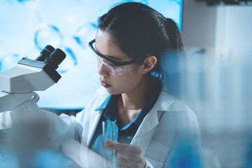 A woman wearing a lab coat and goggles is looking through a microscope