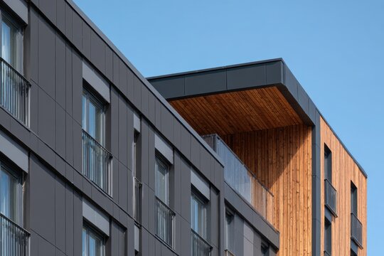 Building facade with black and brown cladding. Dark grey metal cladding with wood panels finish on apartment block. Bottom view. Blue sky. Timber paneling on modern architectural design urban setting