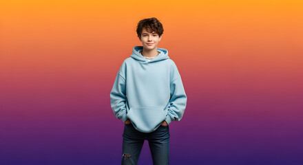 Cheerful teenage boy with a charming smile and curly hair, dressed in a casual blue hoodie and jeans, posing confidently in a studio with a vibrant gradient background