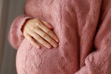 Expectant mother gently cradling her baby bump while wearing a cozy knitted sweater in a serene indoor setting