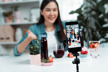Selective focus smartphone with smiling young beautiful Asian reviewing mixed strawberry and cherry juice detox drink, presenting healthy product promotion selling on social media online. Stratagem.