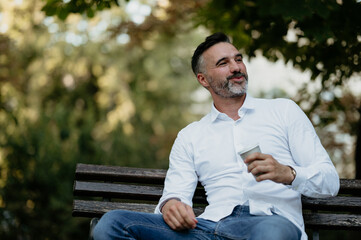 Obraz premium Mature man relaxing on park bench drinking coffee