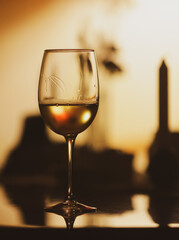Shallow depth of field (selective focus) details with a glass of white wine on a table in a dark room with back light
