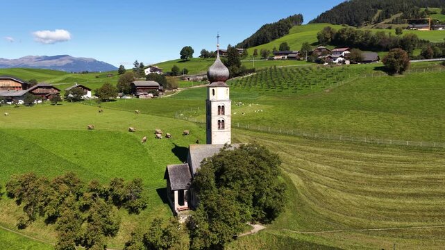 Small church, chiesa in the Italian dolomites. Alpine fields, agricultural grass lands. Aerial video.