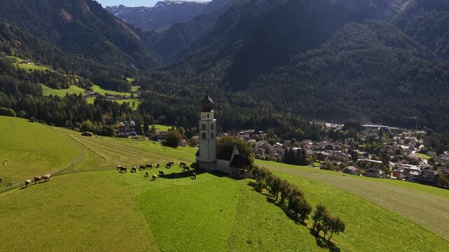 Small church, chiesa in the Italian dolomites. Alpine fields, agricultural grass lands. Aerial video.