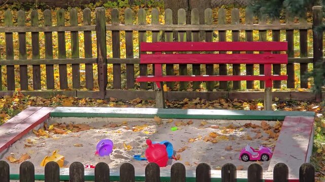 Sunny autumn playground with sandbox and falling yellow leaves