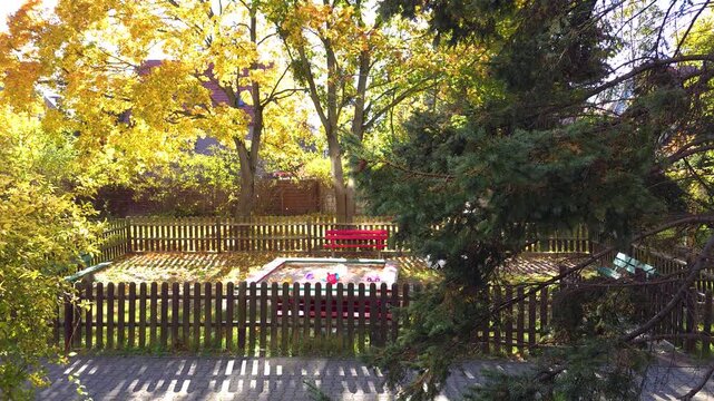 Sunny autumn playground with sandbox and falling yellow leaves