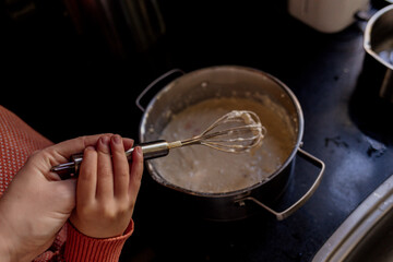 Child and mother whisking batter in metal bowl on kitchen counter