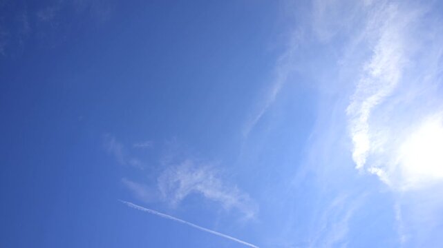 A calm blue sky with a contrail passing by for a moment