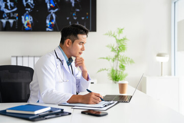 Fototapeta premium Concentrated physician working on computer looking at laptop screen thinking on problem solution concept. Serious doctor wearing white coat doing online research at workplace.