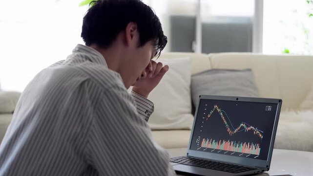 株価の下落を見て落ち込むアジア人男性