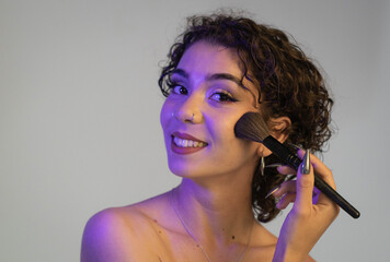 Girl with curly hair applies make-up with a smile. Copy space