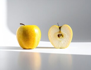 Two yellow apples, one whole, one half, on white surface