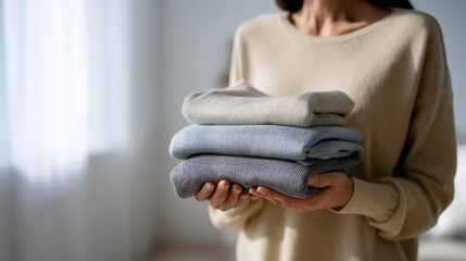 close-up of a woman holding a stack of neatly folded clothes