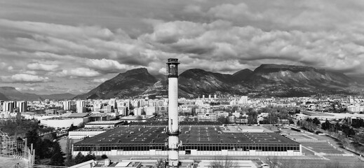 Black and white photo of industrial chimney and city skyline with mountains