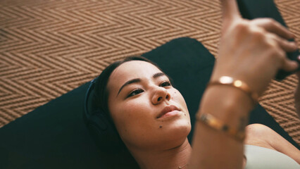 Yoga, headphones and phone with woman on floor for social media, streaming and wellness podcast. Connection, exercise and workout break with above of person in home for fitness, resting and music