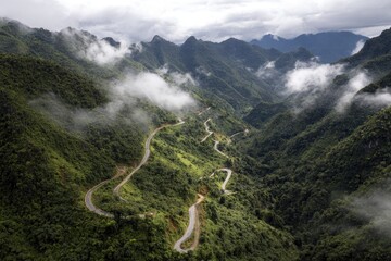 Winding mountain road through lush green valley, shrouded in mist