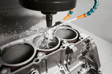 High precision cnc milling machine makes holes in the car engine with a coolant. 