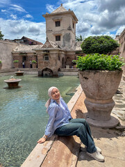 Fototapeta premium Guest enjoys a relaxing moment by the tranquil waters of Taman Sari Water Castle in Yogyakarta