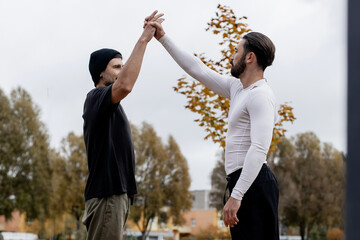 Two young men giving each other a high five outdoors in autumn park, celebrating teamwork and...