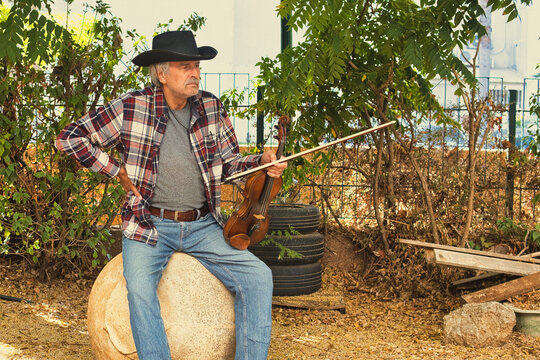 Senior Man in Cowboy Hat Playing the Fiddle Outdoors