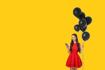 Woman in red dress holds black balloons and uses smartphone