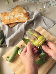 Anonymous person peels artichoke in kitchen at home. Healthy eating and traditional Italian dish. Fresh seasonal farm produce.