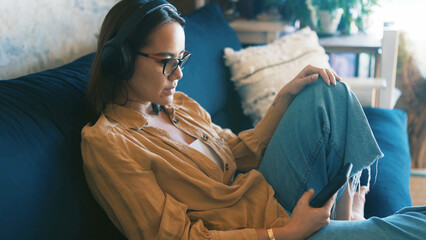 Lounge, smartphone and woman with headphones, chill and listening to music on couch and comfortable. Streaming, audio and person with mobile for song selection, relax and calm with tech in house © peopleimages.com