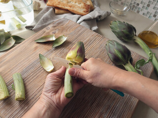 Anonymous person peels artichoke in kitchen at home. Healthy eating and traditional Italian dish. Fresh seasonal farm produce.