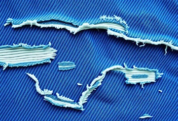 Close-up of distressed denim fabric with visible rips and frayed edges, showing texture and blue tones,  textile background,  frayed