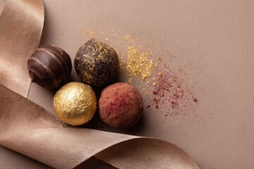 Four chocolate truffles with golden ribbon on brown background, top view