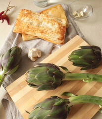 Artichoke flowers and toasted ciabatta bread on kitchen table at home. Healthy eating and traditional Italian cuisine. Seasonal farm products.