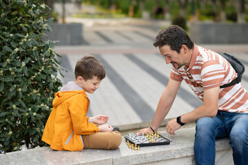 Boy with father playing chess outdoor. Learning strategic game. Education.
