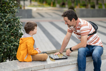 Boy with father playing chess outdoor. Learning strategic game. Education.