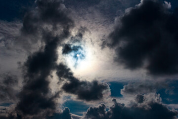 Brilliant sun bursts through a thick veil of ominous, dark clouds, casting an ethereal glow on a turbulent sky. Nature's raw power on display