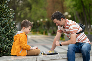 Boy with father playing chess outdoor. Learning strategic game. Education.